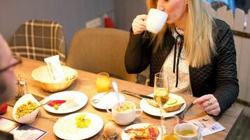 A dining table with breakfast items, a person drinking from a cup, and a modern interior with hanging lights.