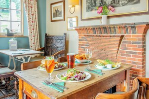 Un comedor rústico con chimenea de ladrillo, muebles de madera y una mesa dispuesta con platos de comida y bebidas.