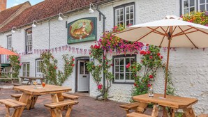 A white building with a sign reading "The Tiger Inn" and a brick patio with wooden picnic tables and an umbrella. - Patience - Tiger Inn (Eastbourne)