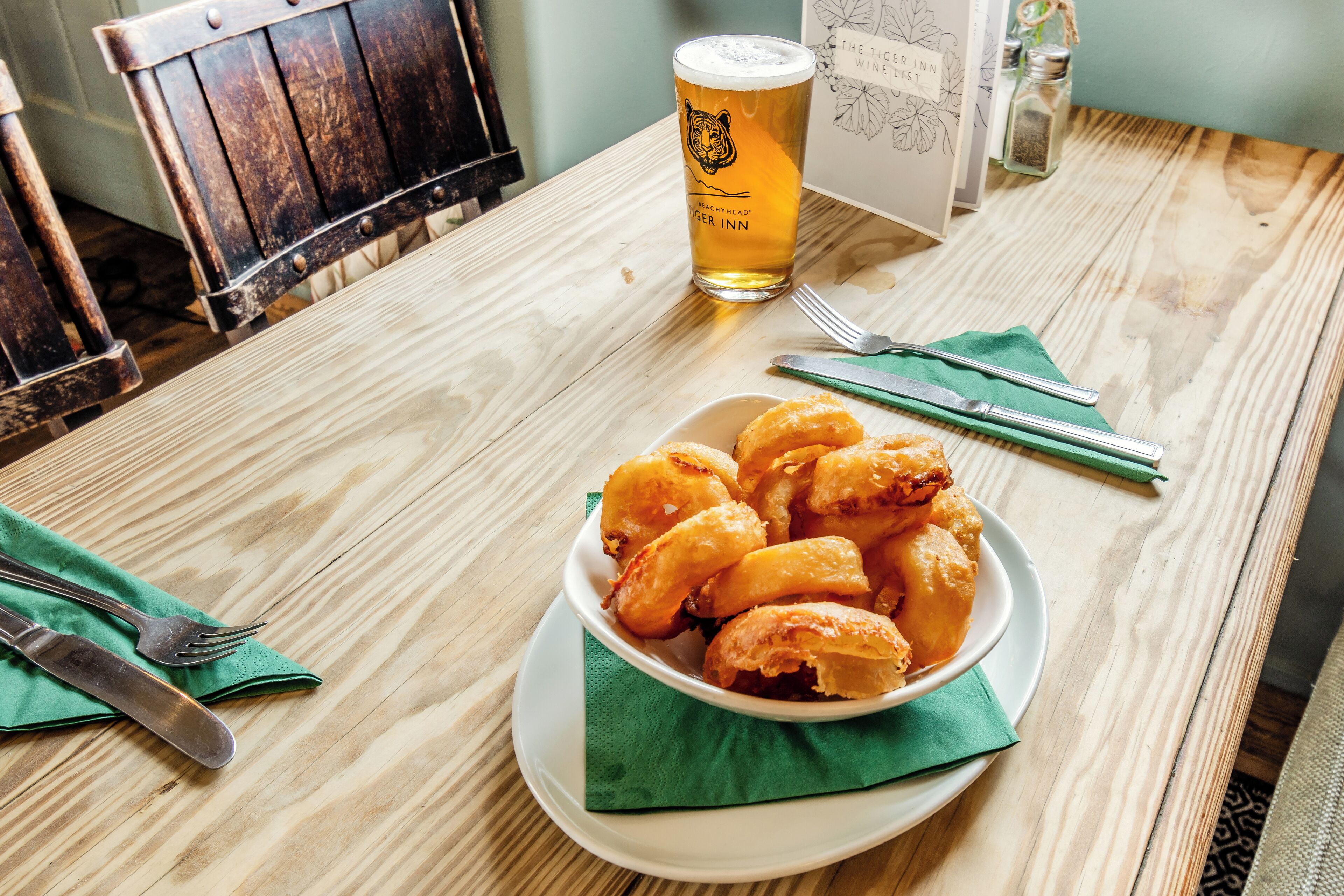 Un tavolo di legno con una ciotola di cibo fritto, un bicchiere di birra e posate.