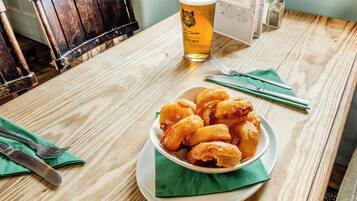 Un tavolo di legno con una ciotola di cibo fritto, un bicchiere di birra e posate.