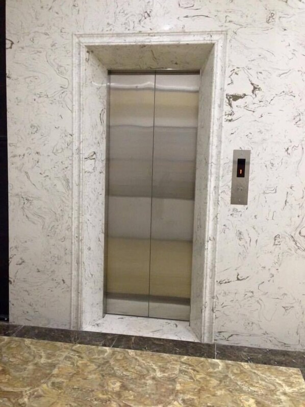 Un ascensor con pared y suelo de mármol, con un diseño sencillo y un panel de control a la derecha.