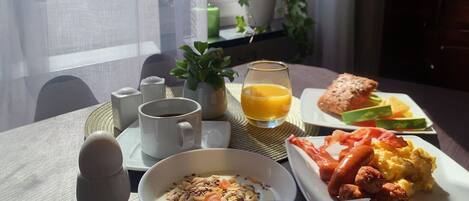 A breakfast setting with a bowl of cereal, a plate of eggs, toast, and juice on a table by a window.