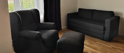 A room with a sofa, a chair, and a window with curtains.