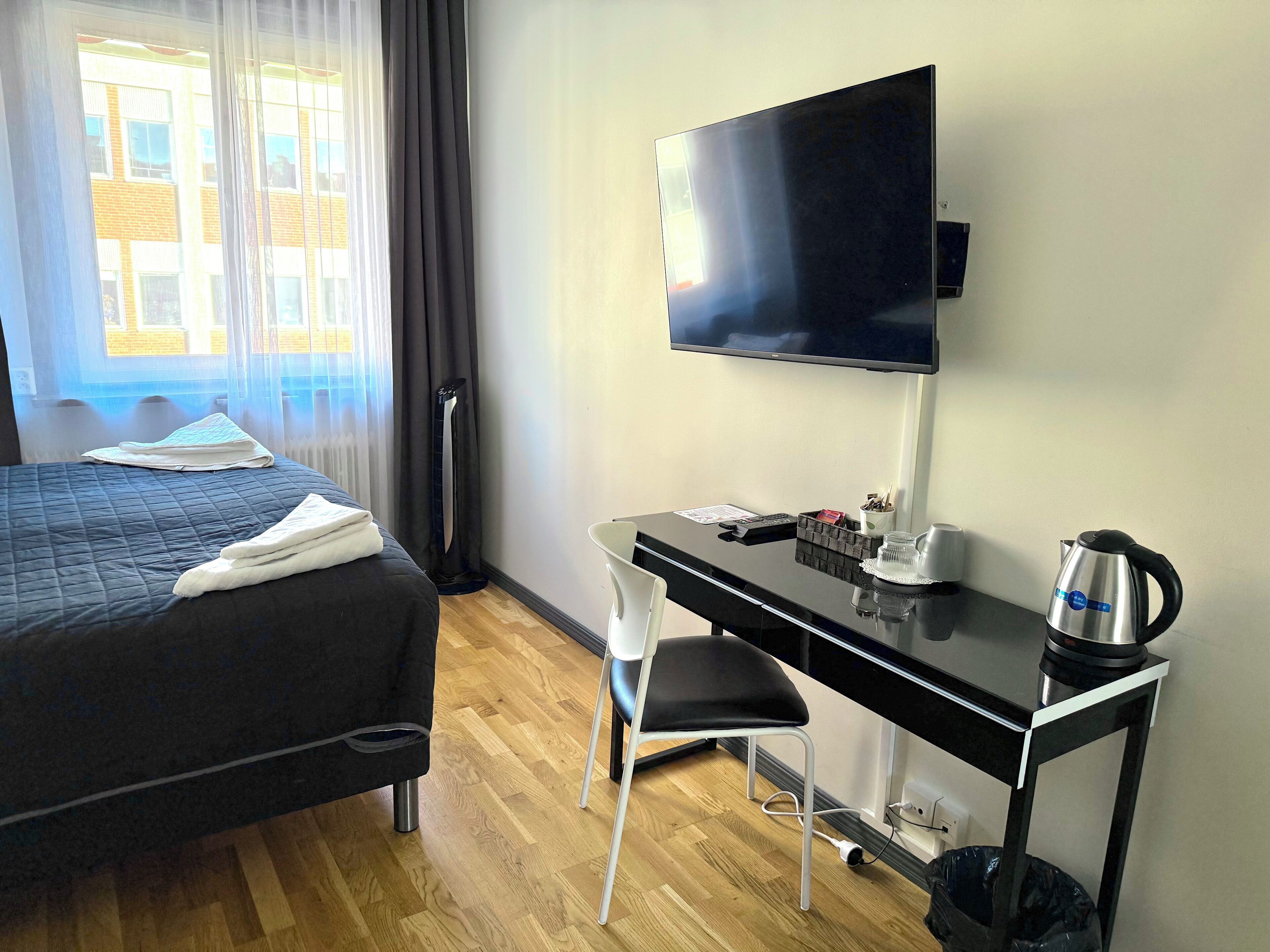 A hotel room with a bed, a desk with a chair, a television, and a kettle.