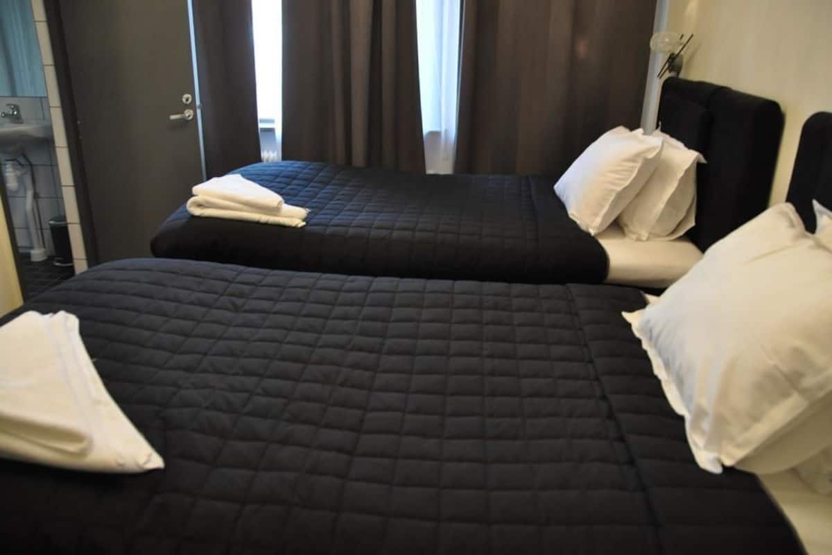 Hotellihuone, jossa on kaksi sänkyä. Kummassakin sängyssä on musta, tikattu peitto ja valkoiset tyynyt.
