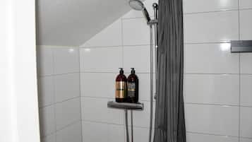 A shower area with a showerhead, a shower curtain, and two bottles of shampoo on a shelf.