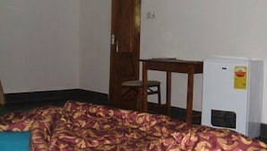 Een kamer met een bed, een houten bureau, een stoel en een witte koelkast.