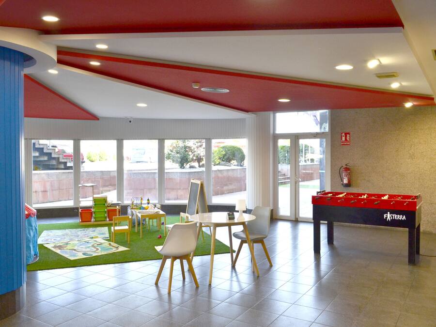Un espacio interior amplio con mesa de fútbol, una pequeña zona de juegos con juguetes y un extintor en la pared.