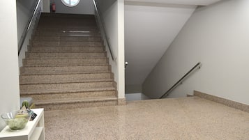A staircase with a handrail, a fire extinguisher, and a small table with a bowl on the landing.
