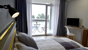 Habitación de hotel con cama, escritorio con televisor, una silla y balcón con mesa y sillas.