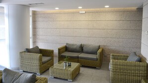 Un área de descanso moderna con mobiliario de mimbre, incluyendo sofás y sillones, dispuestos alrededor de una mesa central.