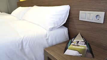 A neatly made bed with white linens, a wooden headboard, and a bedside table with a brochure.