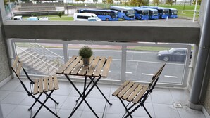 Un balcón con mesas y sillas de madera, con vista a un estacionamiento con autobuses y una carretera.