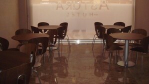 Interior de un restaurante con mesas y sillas redondas, un ventanal con vistas a edificios, y un letrero que dice 'AUSTRA RESTAURANT'.
