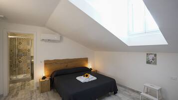Ein Schlafzimmer mit Dachfenster, einem Bett mit dunkler Bettdecke, einem Nachttisch mit Lampe und einem kleinen weißen Tisch.