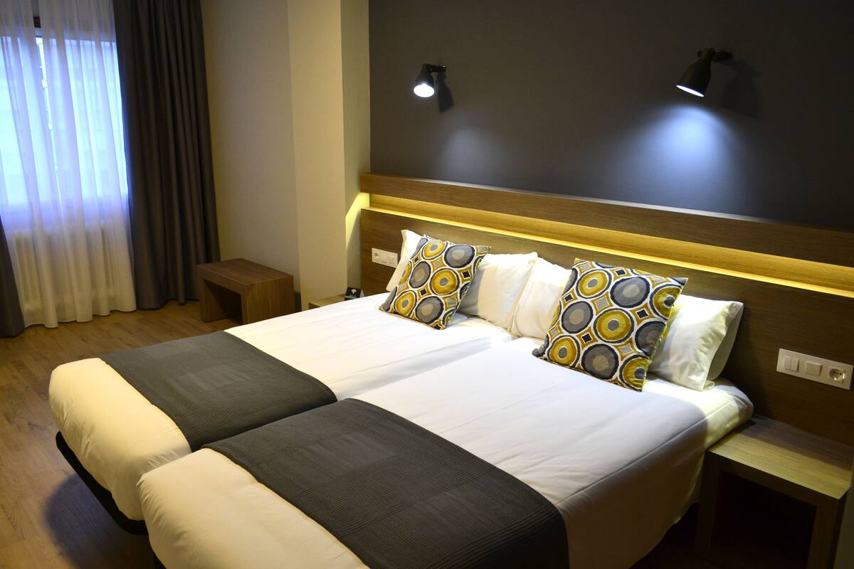Un lit double avec deux oreillers, une table de chevet et une lampe fixée au mur.