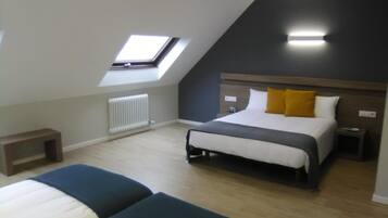 Een slaapkamer met een schuine plafond, dakraam, bed met wit en geel beddengoed, nachtkastje en een nachttafel.