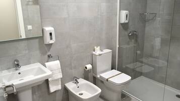 Un baño moderno con lavabo, bidé, inodoro y ducha con mampara de vidrio.