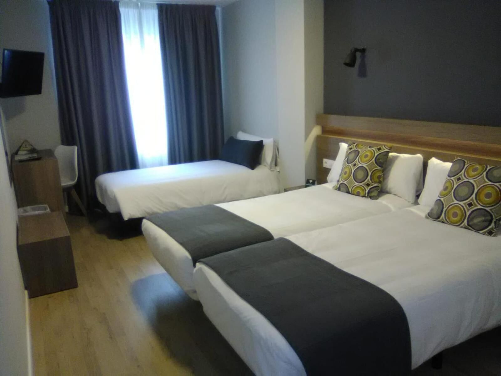 Quarto de hotel com duas camas, televisão de tela plana, escrivaninha e janela com cortinas.