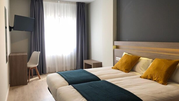 Een hotelkamer met een groot bed, een bureau, een televisie en een raam met gordijnen.