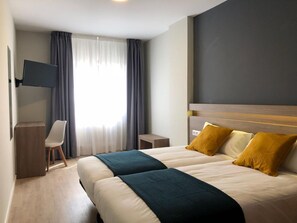 Une chambre d’hôtel avec un grand lit, un bureau, une télévision et une fenêtre avec des rideaux.