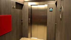 Un ascensor con interior metálico, un letrero rojo de salida de emergencia y un indicador de piso.