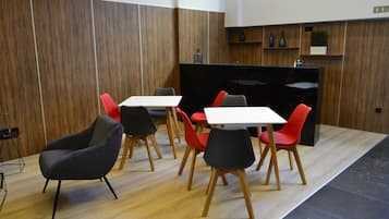 Un comedor moderno con paneles de madera, encimera negra y una combinación de sillas rojas y negras alrededor de mesas blancas.