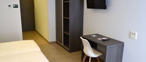 Una habitación de hotel con una cama, un escritorio con silla, un armario y un televisor montado en la pared.