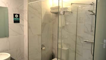 A modern bathroom with a glass-enclosed shower, a marble-tiled wall, and a toilet with a paper towel dispenser.