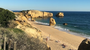 A beach with rocky cliffs, clear blue sky, and calm sea. - Rio Apartments (Loulé)