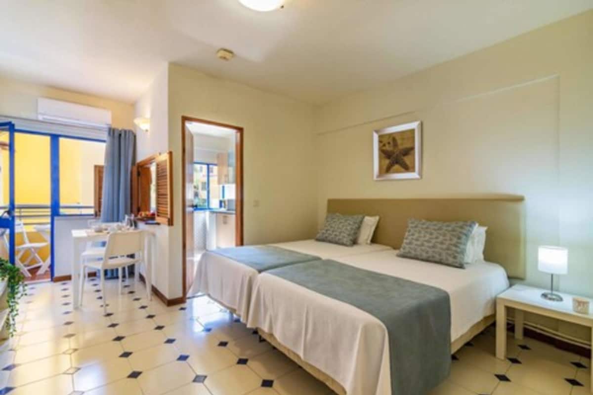 Quarto de hotel com duas camas, uma escrivaninha e uma cadeira.