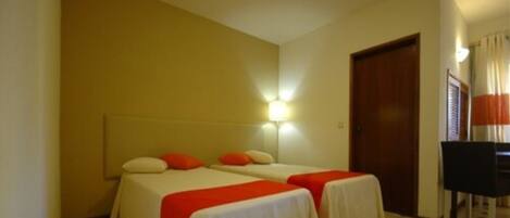A hotel room with two beds, a desk, and a chair.