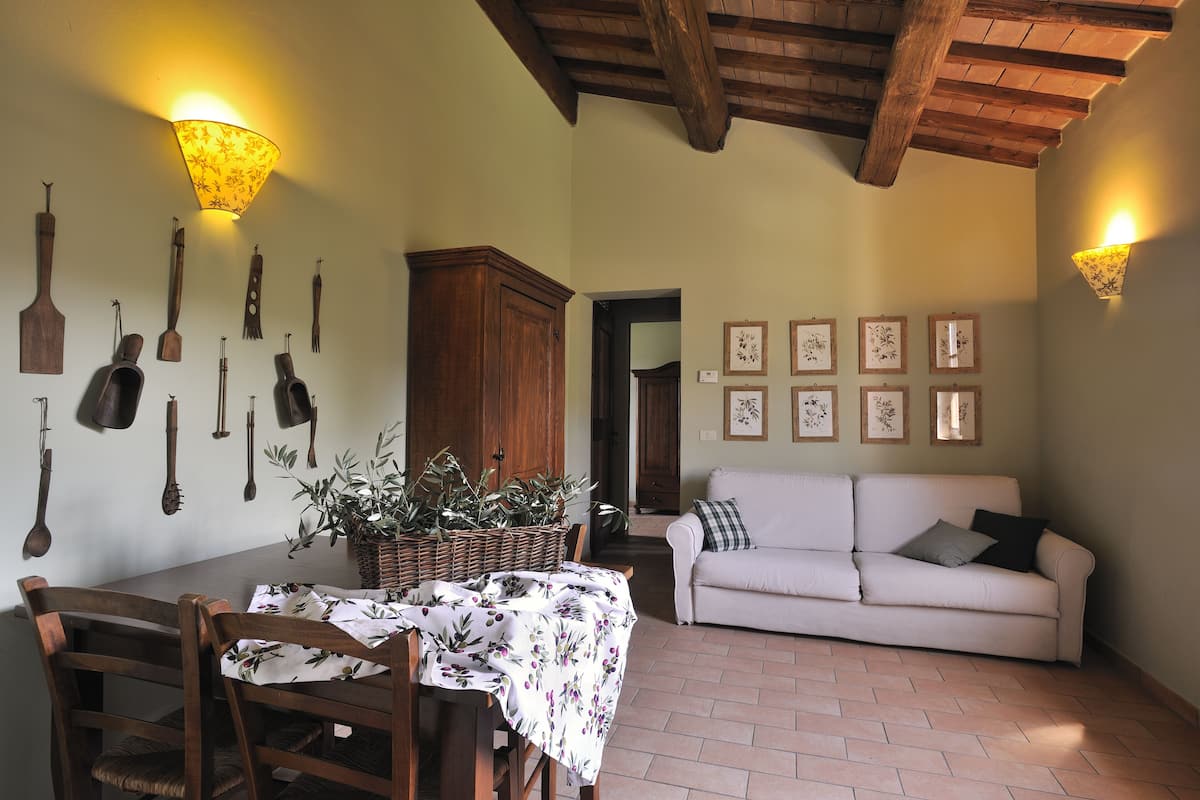 A dining area with a table set for two, a white sofa, and a wall decorated with framed pictures.