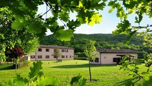 Un grand bâtiment avec un jardin à l’avant, entouré d’arbres et de collines.
