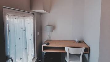 A small, compact room with a wooden ceiling, a desk with a chair, a window with curtains, and a lamp.