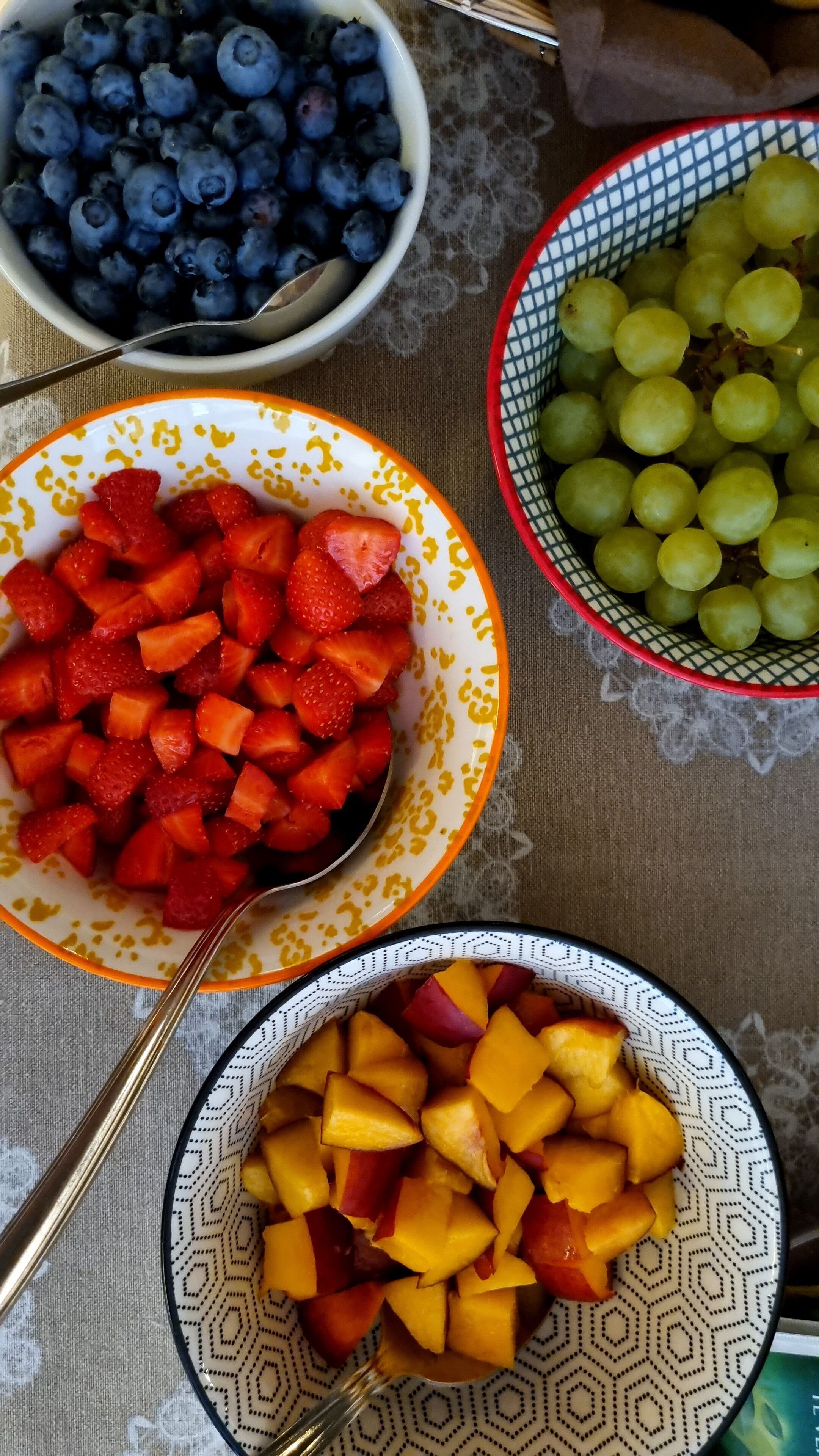 Een tafel met schalen vol fruit, waaronder bosbessen, aardbeien, druiven en mango's.