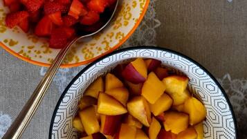 Een tafel met schalen vol fruit, waaronder bosbessen, aardbeien, druiven en mango's.