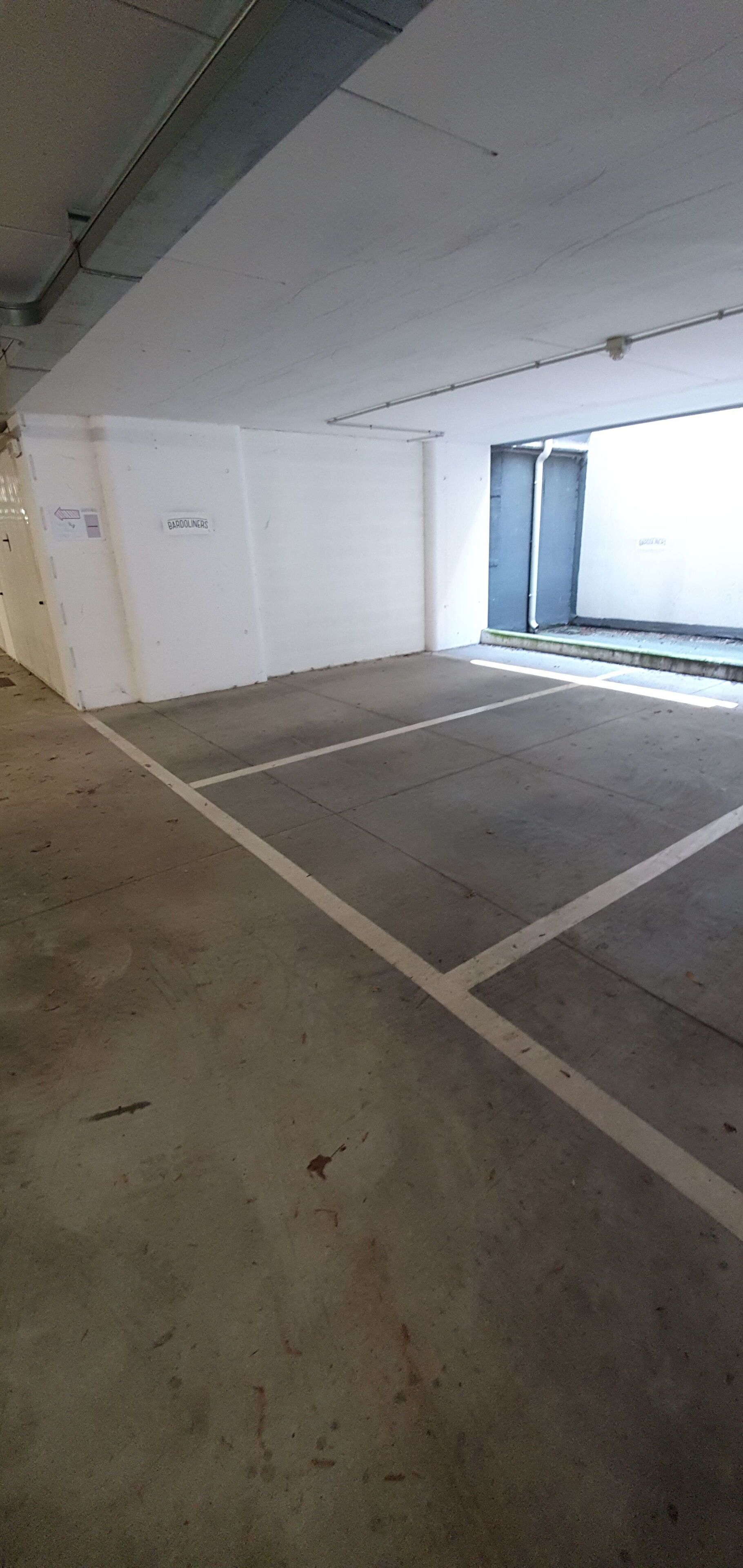 A parking garage with white walls and concrete floors, marked parking spaces, and a visible exit door.
