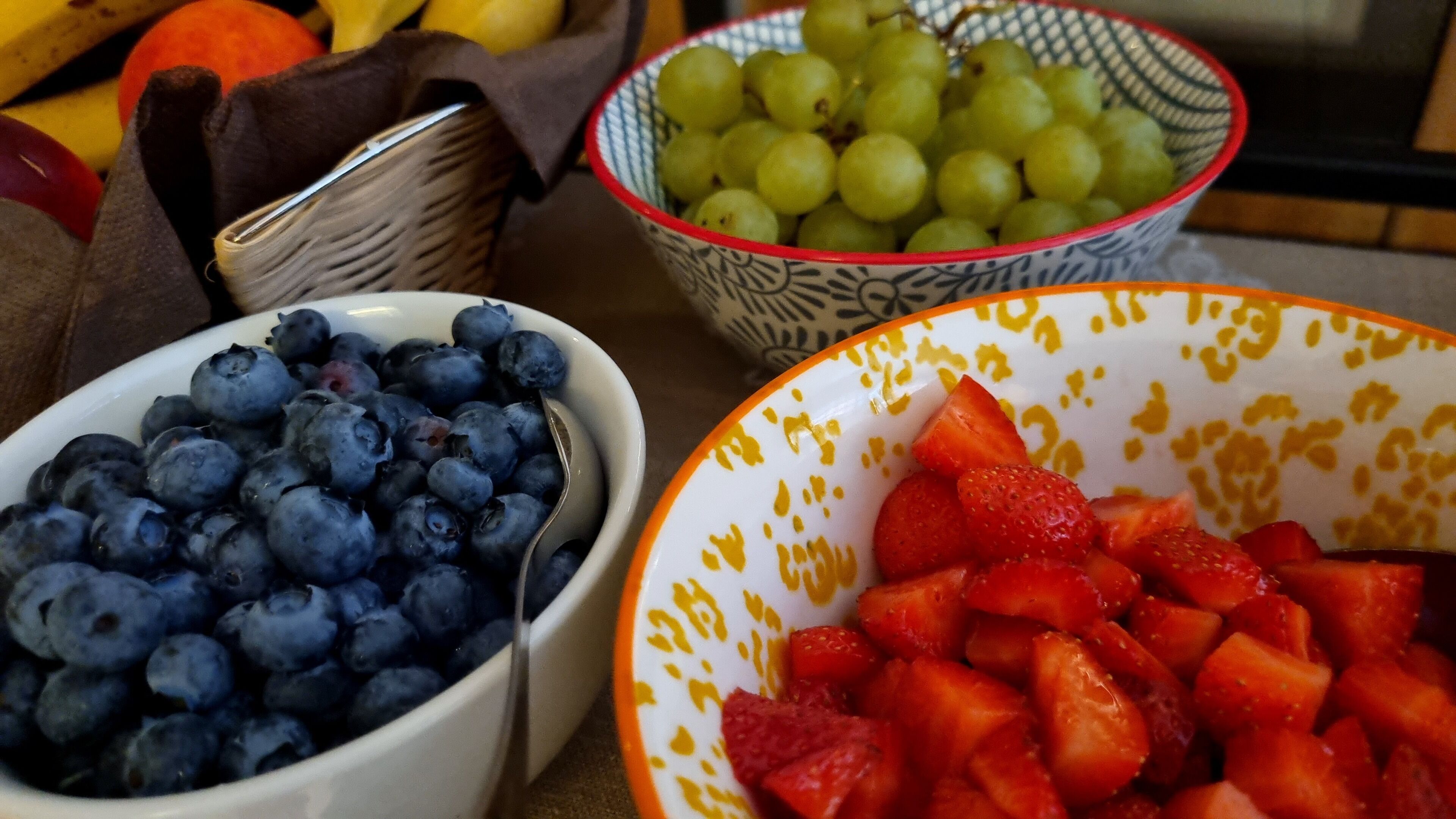Three bowls of fruit: blueberries, grapes, and strawberries.