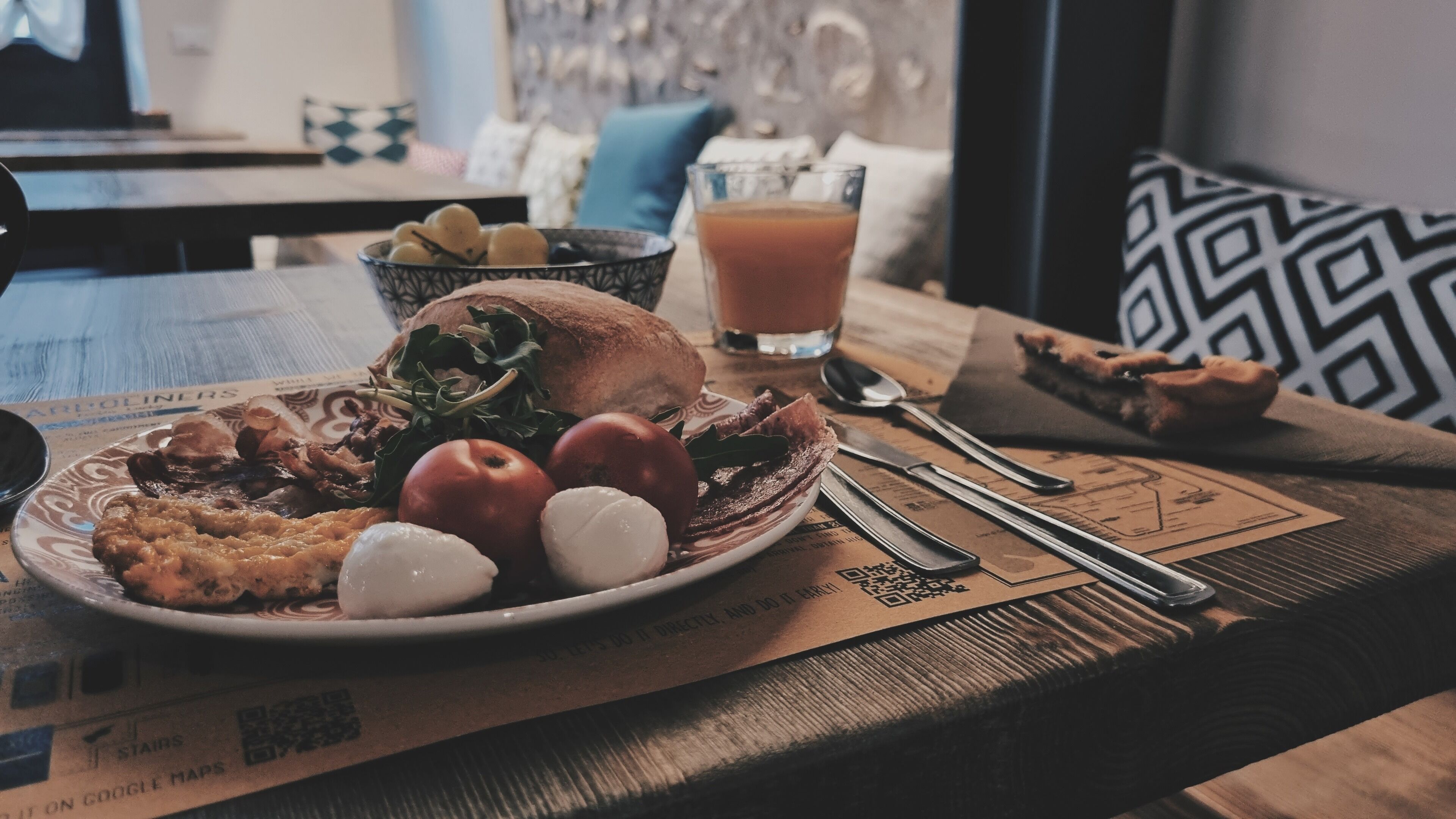 Une table en bois dressée pour le petit-déjeuner, avec une assiette de nourriture, un verre de jus et des couverts.