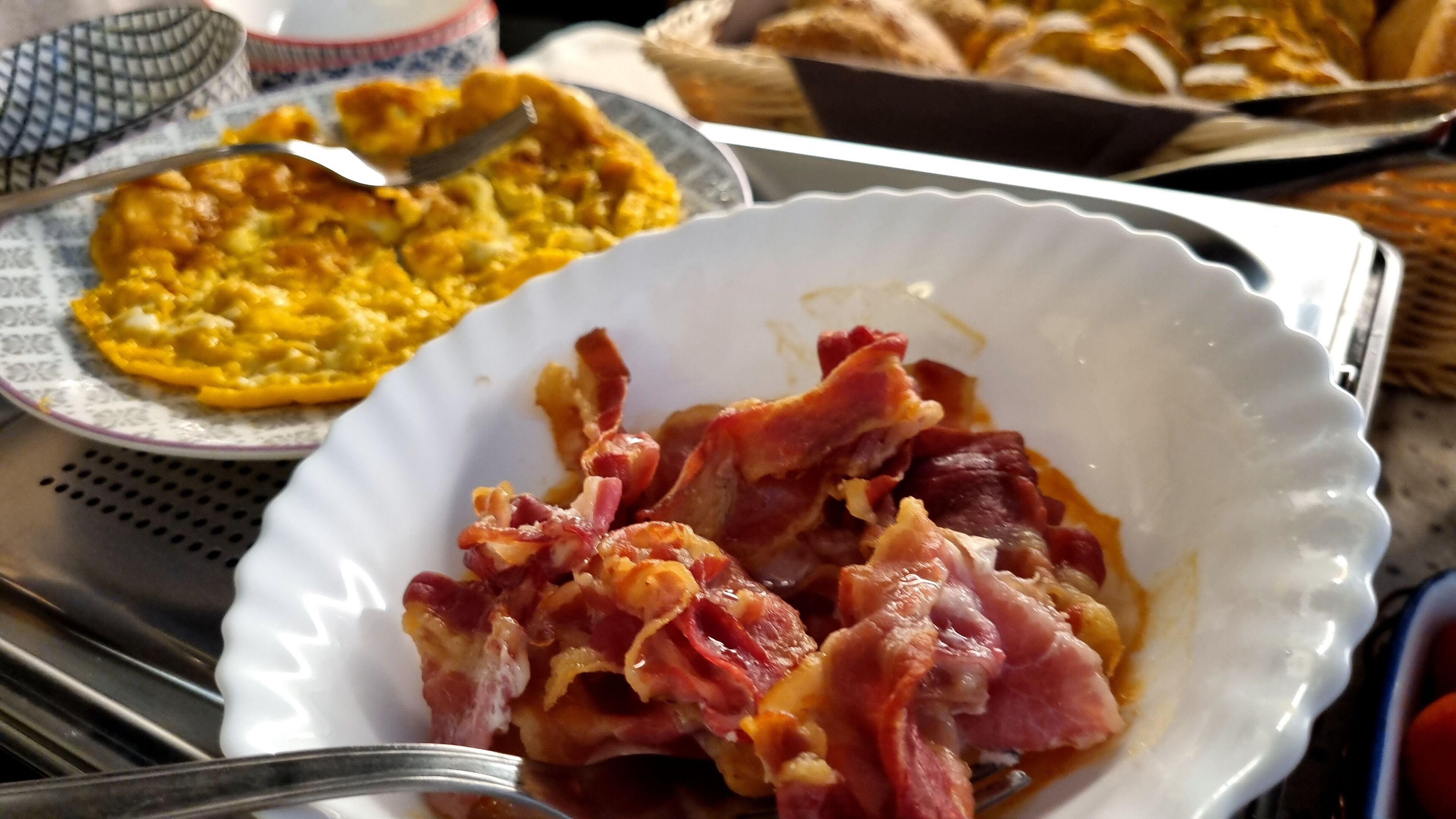 A breakfast setting with a plate of scrambled eggs and bacon, a bowl of fruit salad, and a basket of bread.