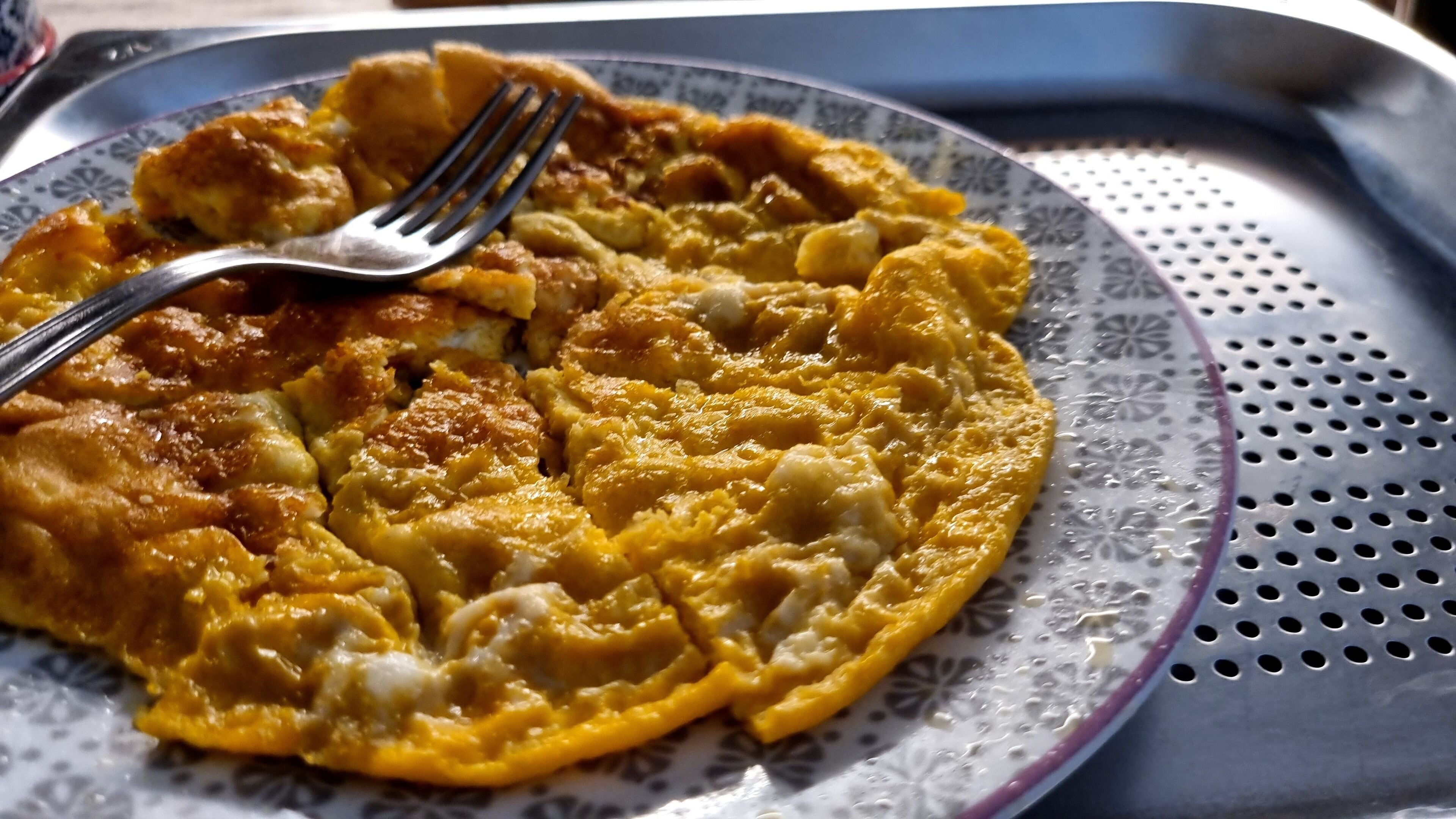 Un piatto con un alimento, forse una frittata, e una forchetta su un piatto decorato.