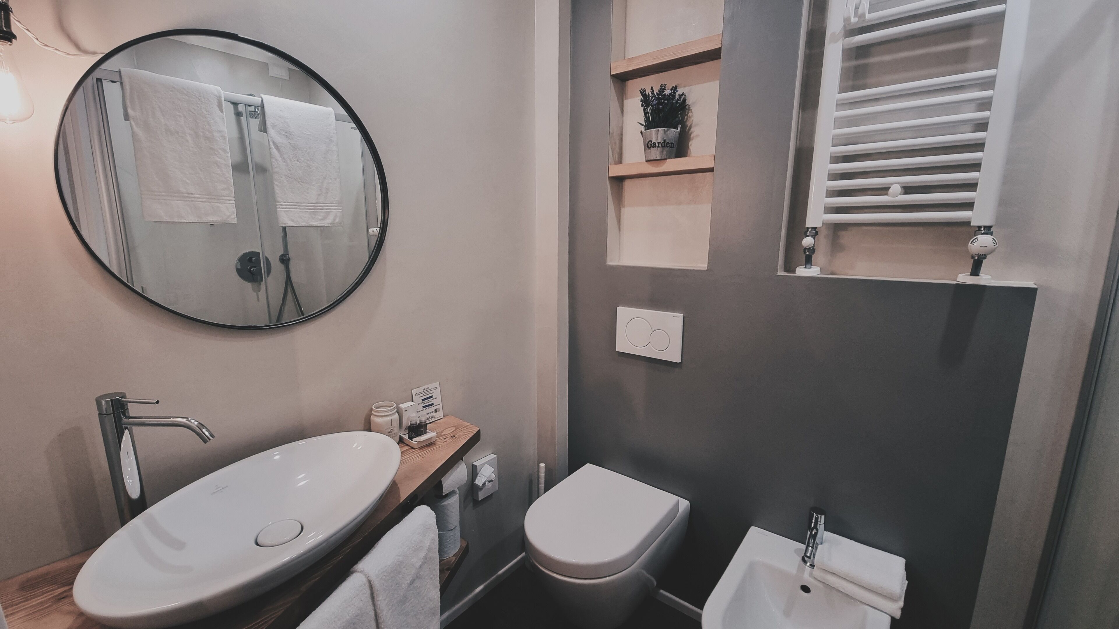 Une salle de bain moderne avec un grand miroir rond, un lavabo, des toilettes et un porte-serviettes.