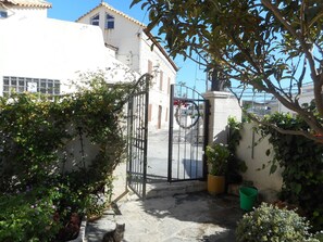 A gated courtyard with a white building, a metal gate, and a potted plant. - Agioklima (Heraklion)