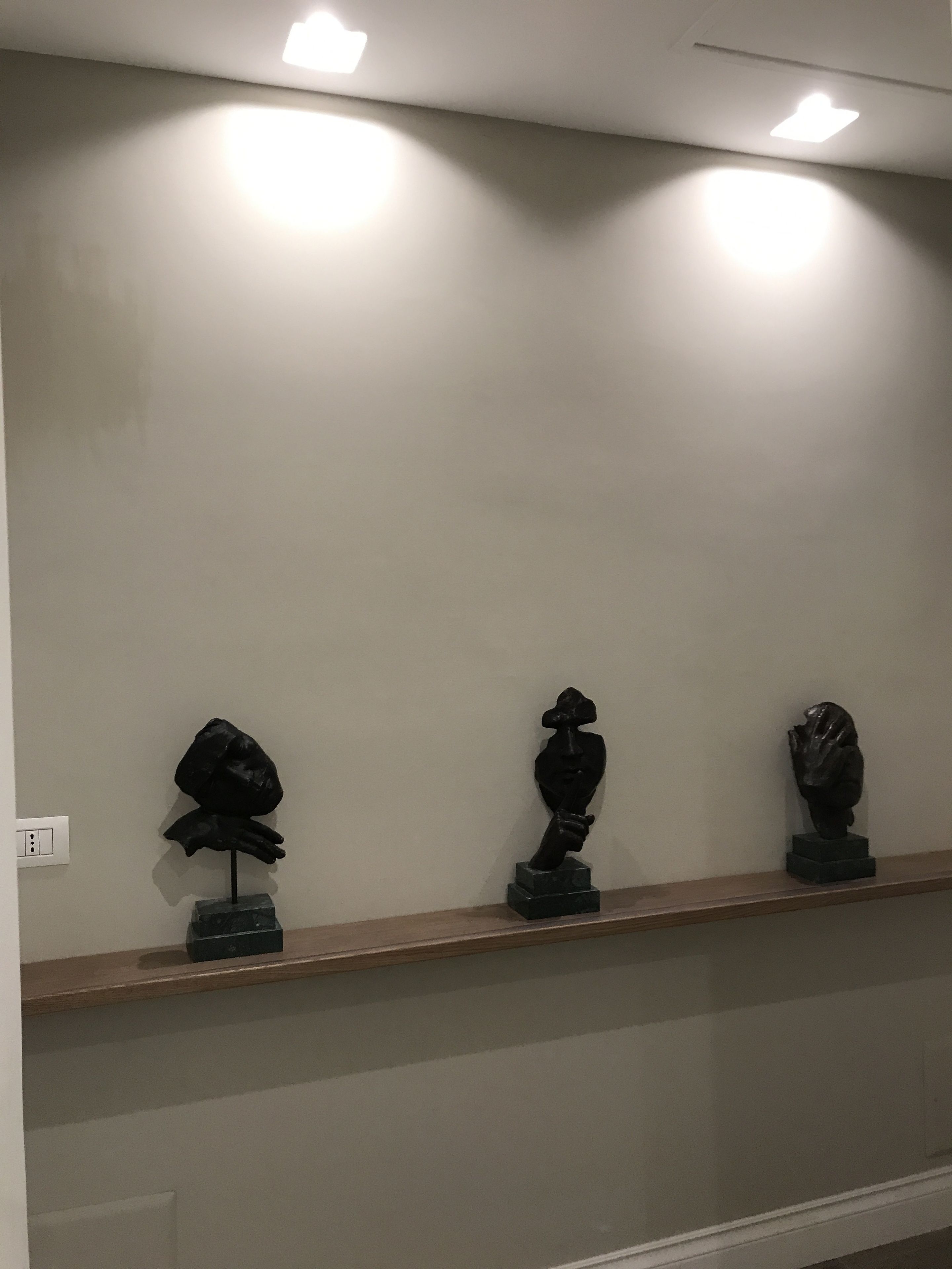 A hallway with a wooden shelf displaying three sculptures.