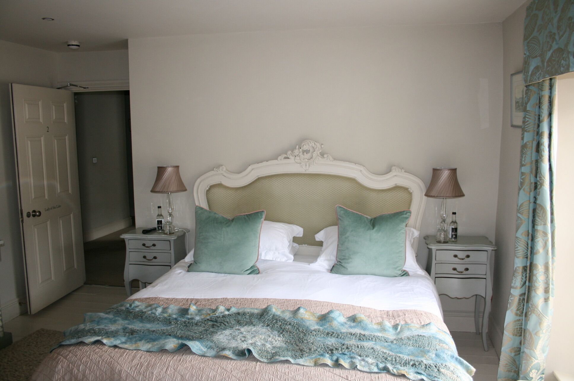 A bedroom with a bed, two bedside tables, a nightstand, a door, and a curtain.