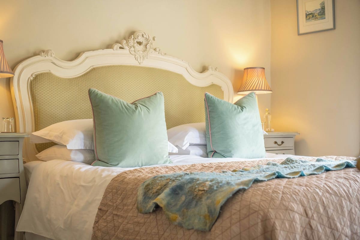 Una cama bien hecha con cubrecolcha acolchada, dos almohadas y un cabecero decorativo.
