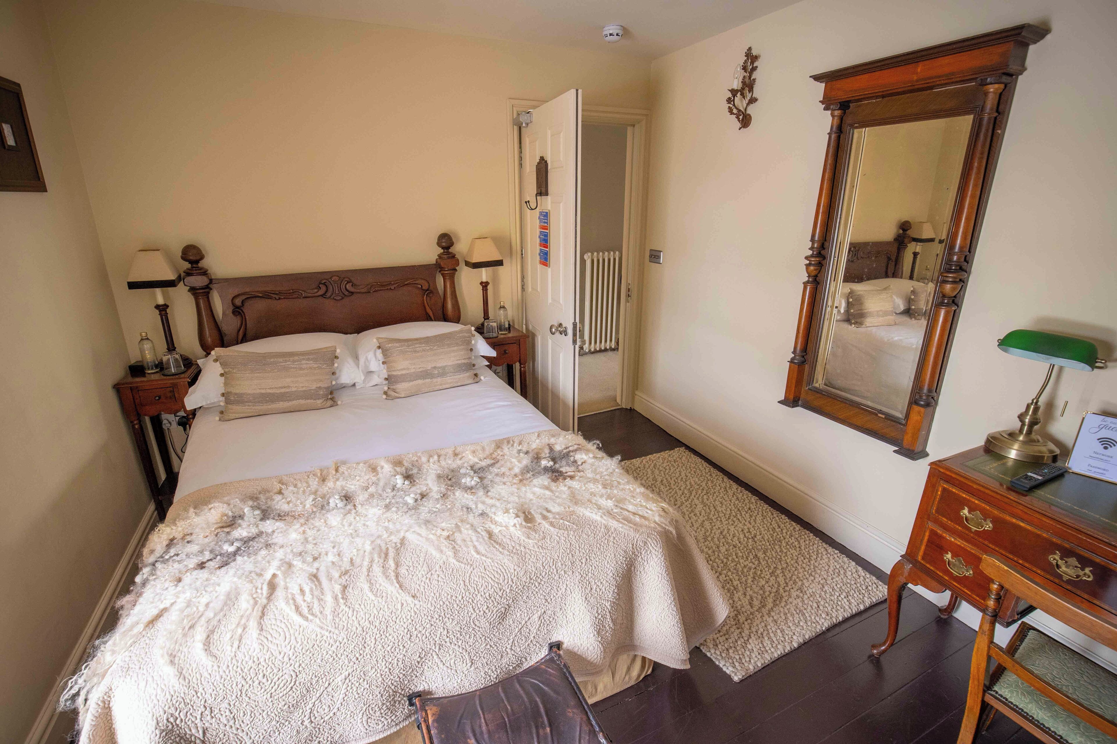 A bedroom with a large bed, a wooden dresser, a mirror, and a radiator.