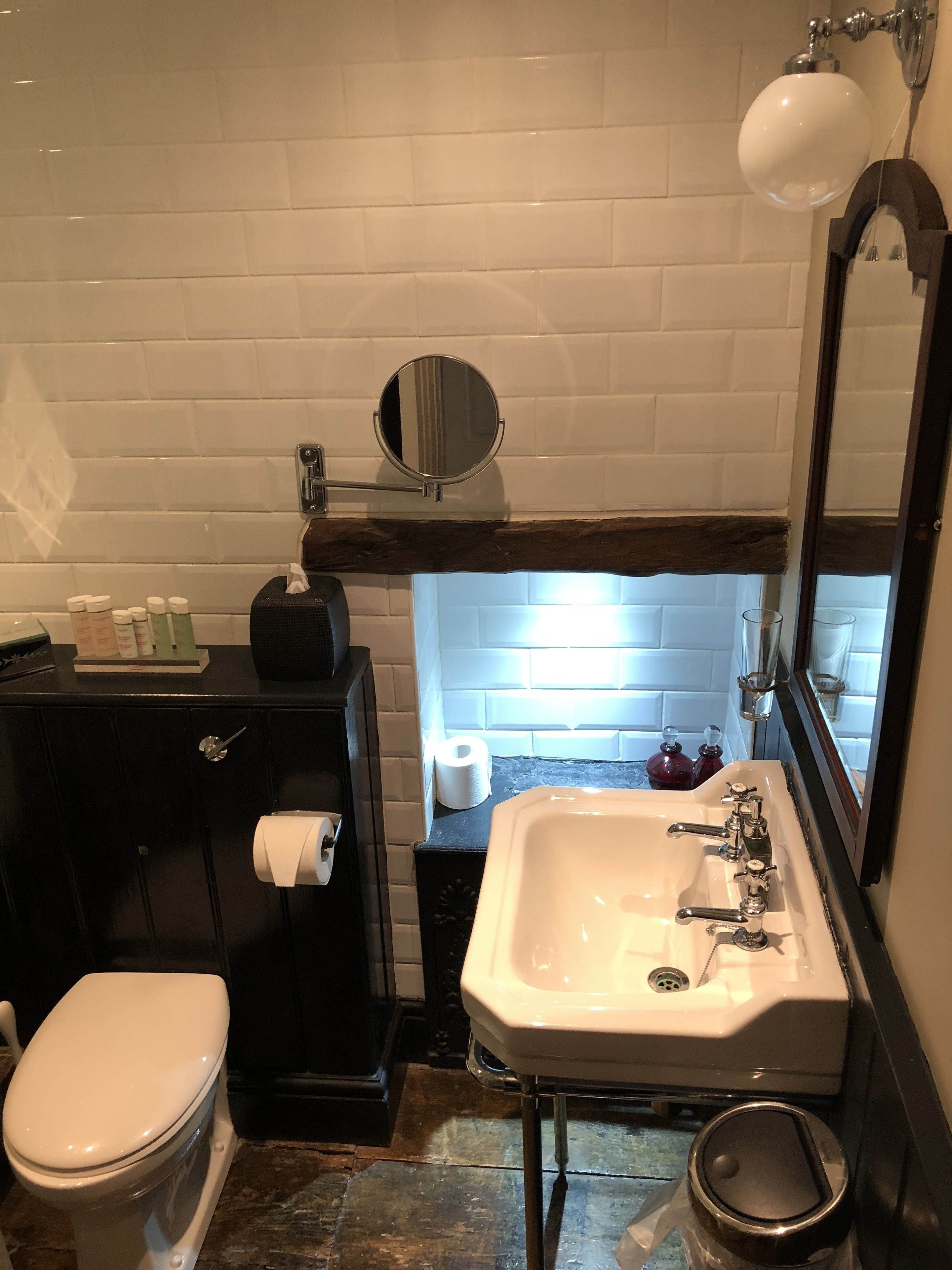 A bathroom with a white sink, toilet, and mirror. There is a black cabinet with toiletries and a towel rack.